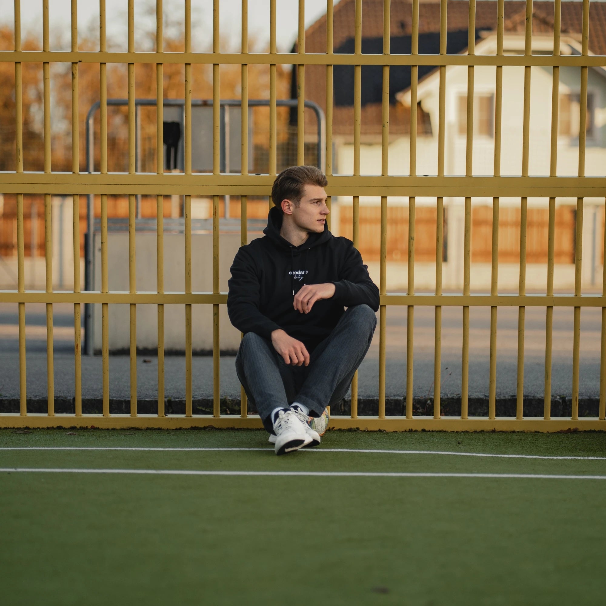 Tobias Anselm am Fußballplatz angelehnt an ein Gitter.